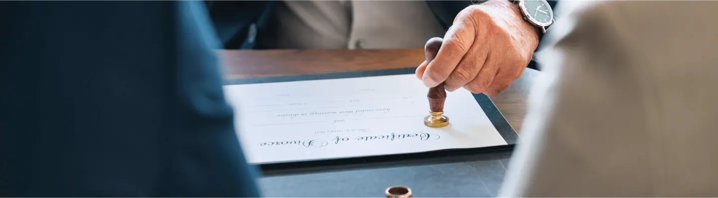 A hand pressing a rubber stamp onto a signed document on a desk