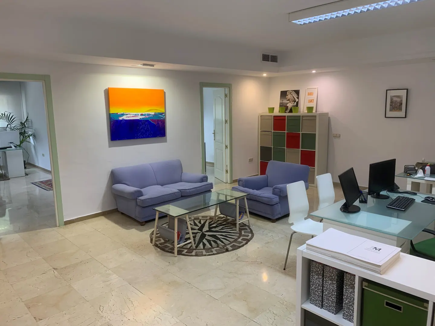 Reception area with two blue sofas, a glass coffee table and desks with computer screens