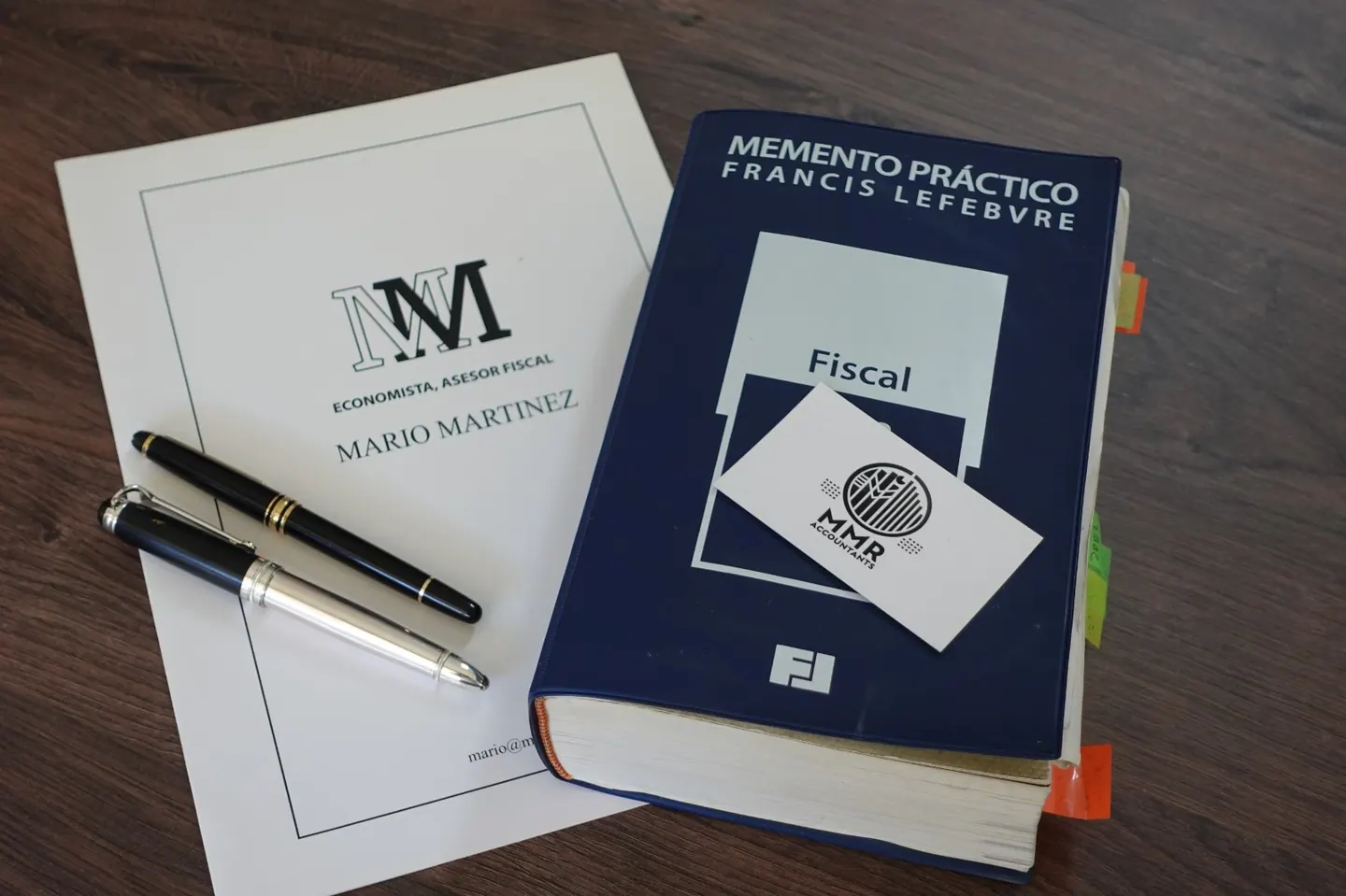 A folder printed with "Mario Martinez, economista, asesor fiscal", two pens, a Memento Práctico Fiscal tax handbook and an MMR business card on a wooden table